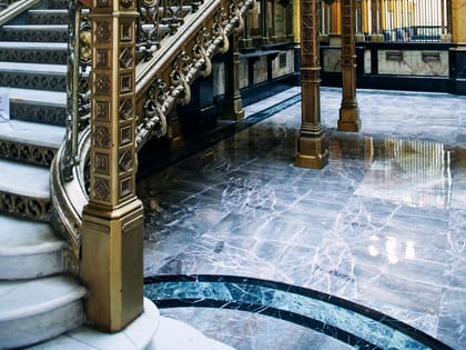Escalier d'honneur en fer forgé doré et sol de marbre dans le hall d'un établissement bancaire ancien.